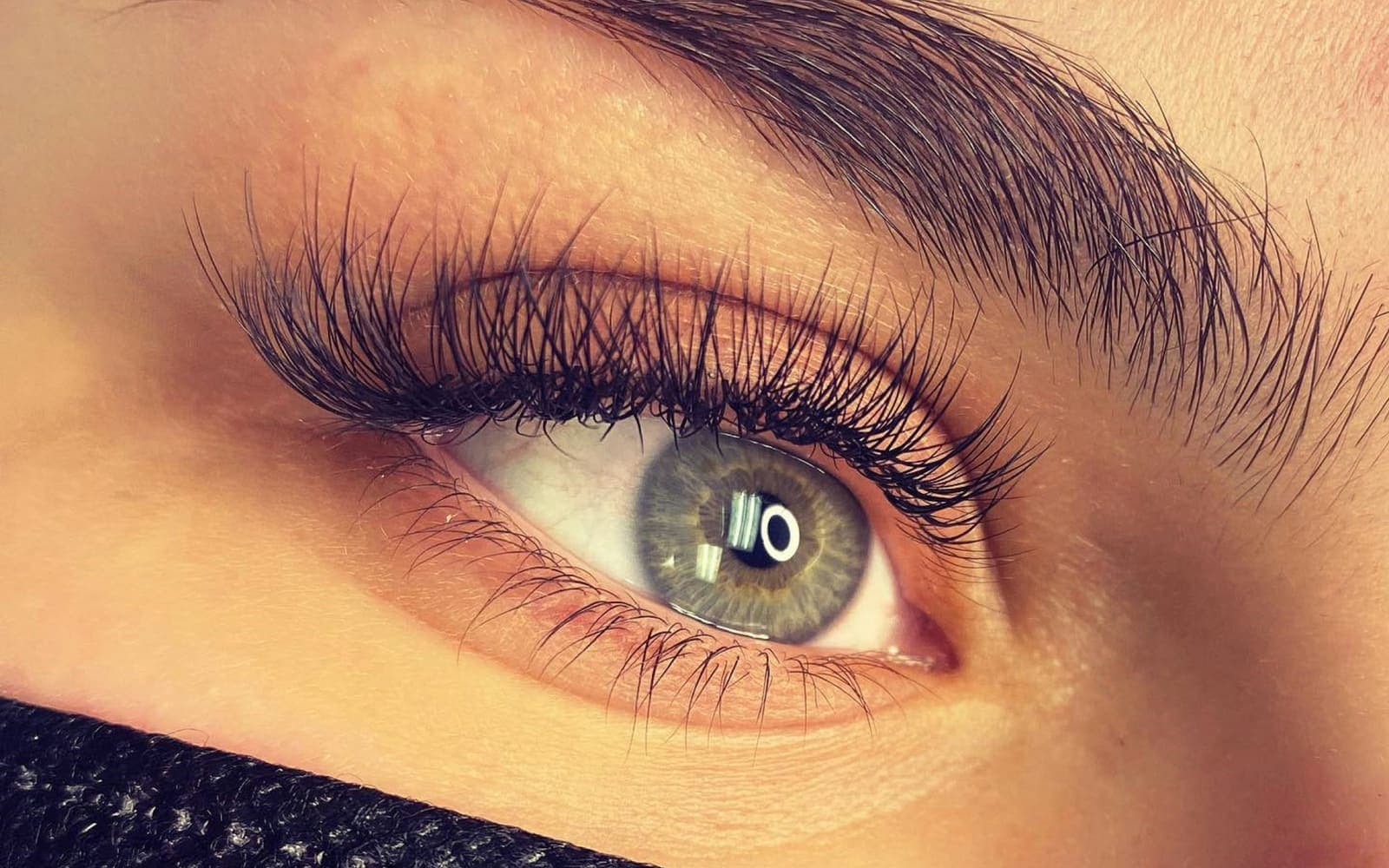 A close-up of an eye wearing a full set of individual lash extensions, fanned and evenly mapped
