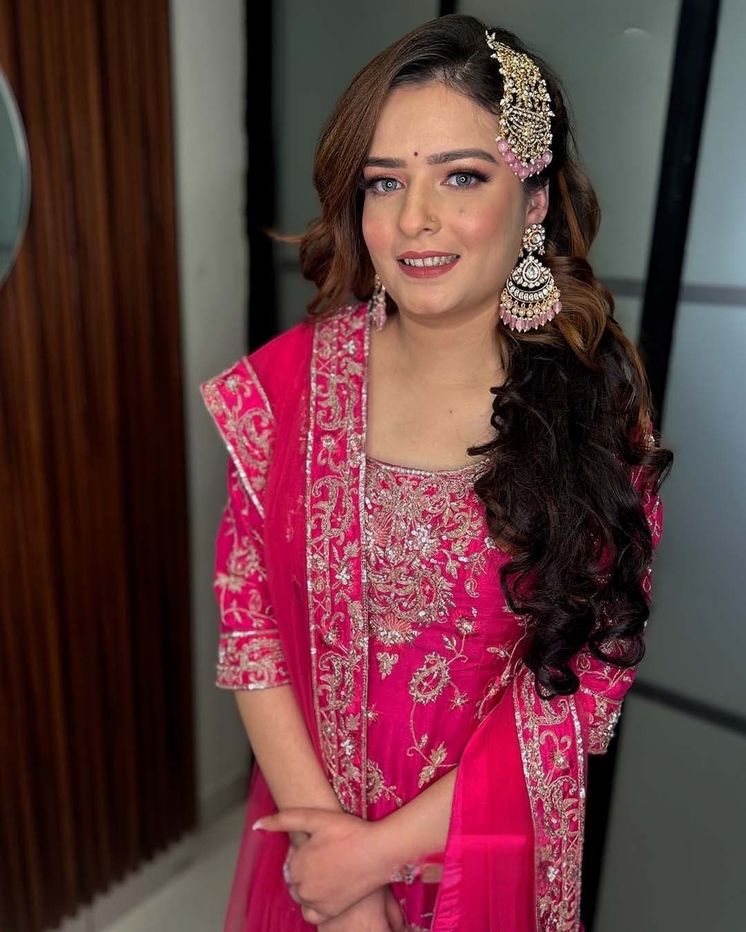 A bride in fuchsia with a maang tikka and soft curls