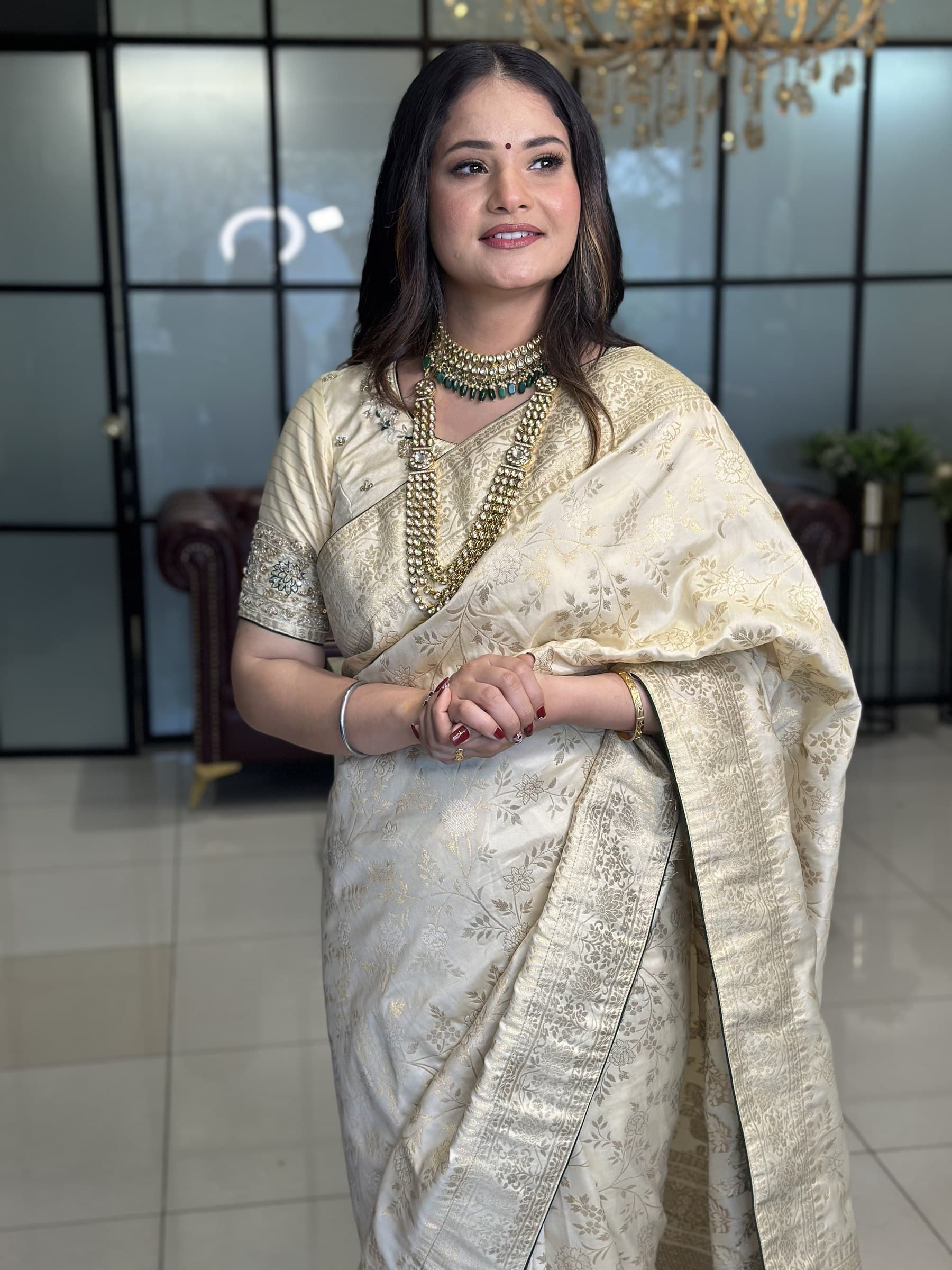 A bride in an ivory tissue saree with a green stone necklace