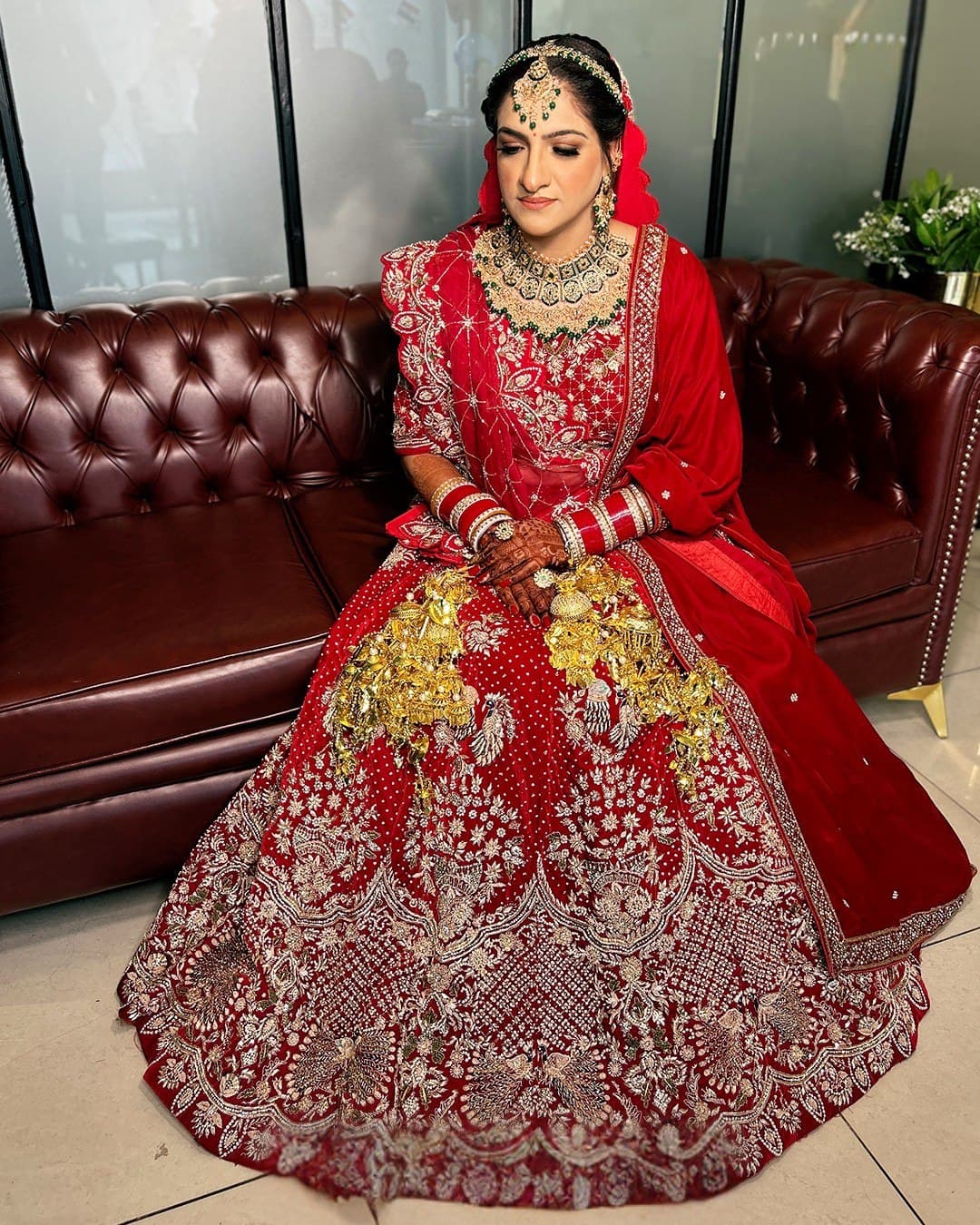 A bride in red seated on a leather couch, kaleere at her wrist