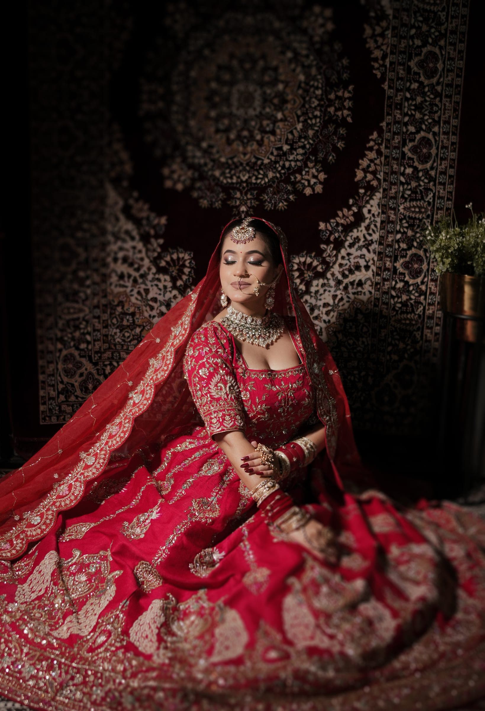 A bride seated in red against a carpet backdrop