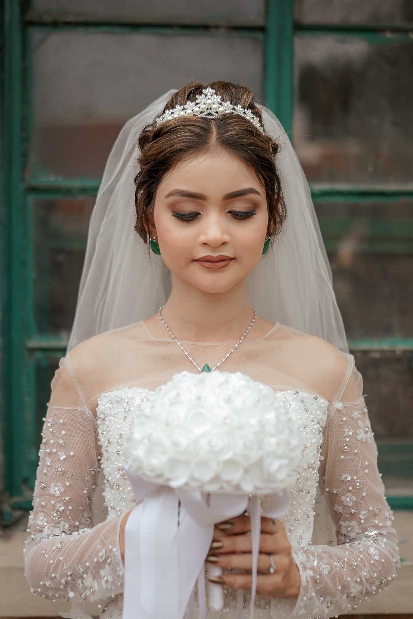 A bride in a white gown and veil holding a white rose bouquet