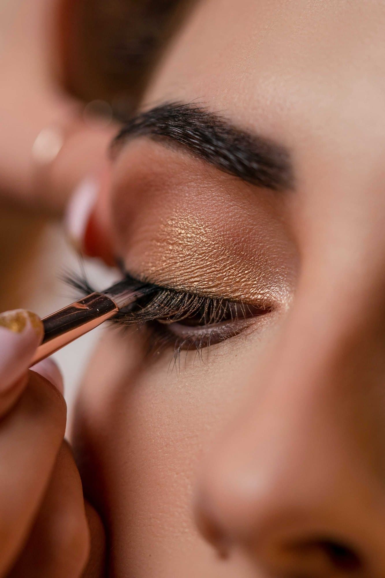 A gold shadow being brushed onto a closed eyelid