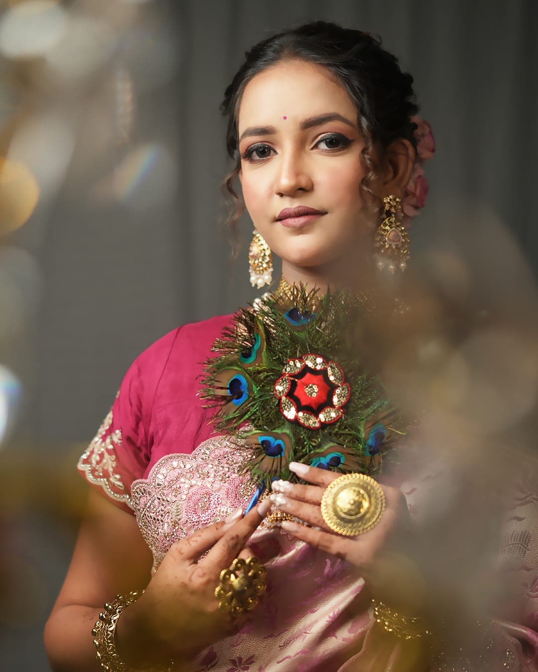 A bride in a pink saree holding a peacock fan
