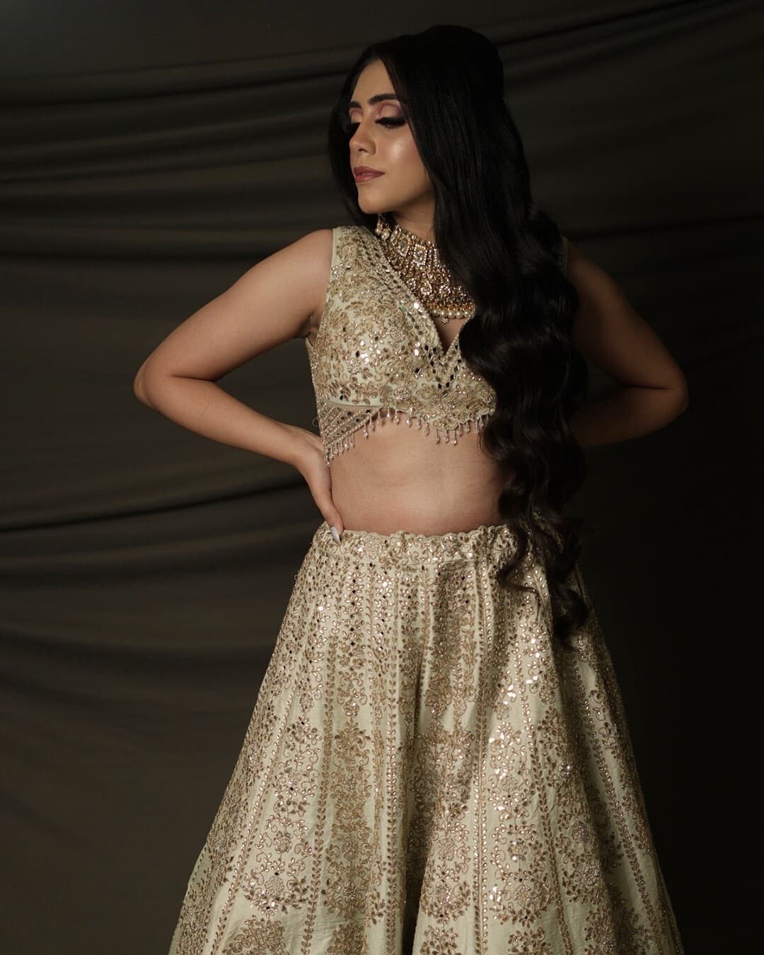 A bride in an ivory mirror-work lehenga against a dark drape