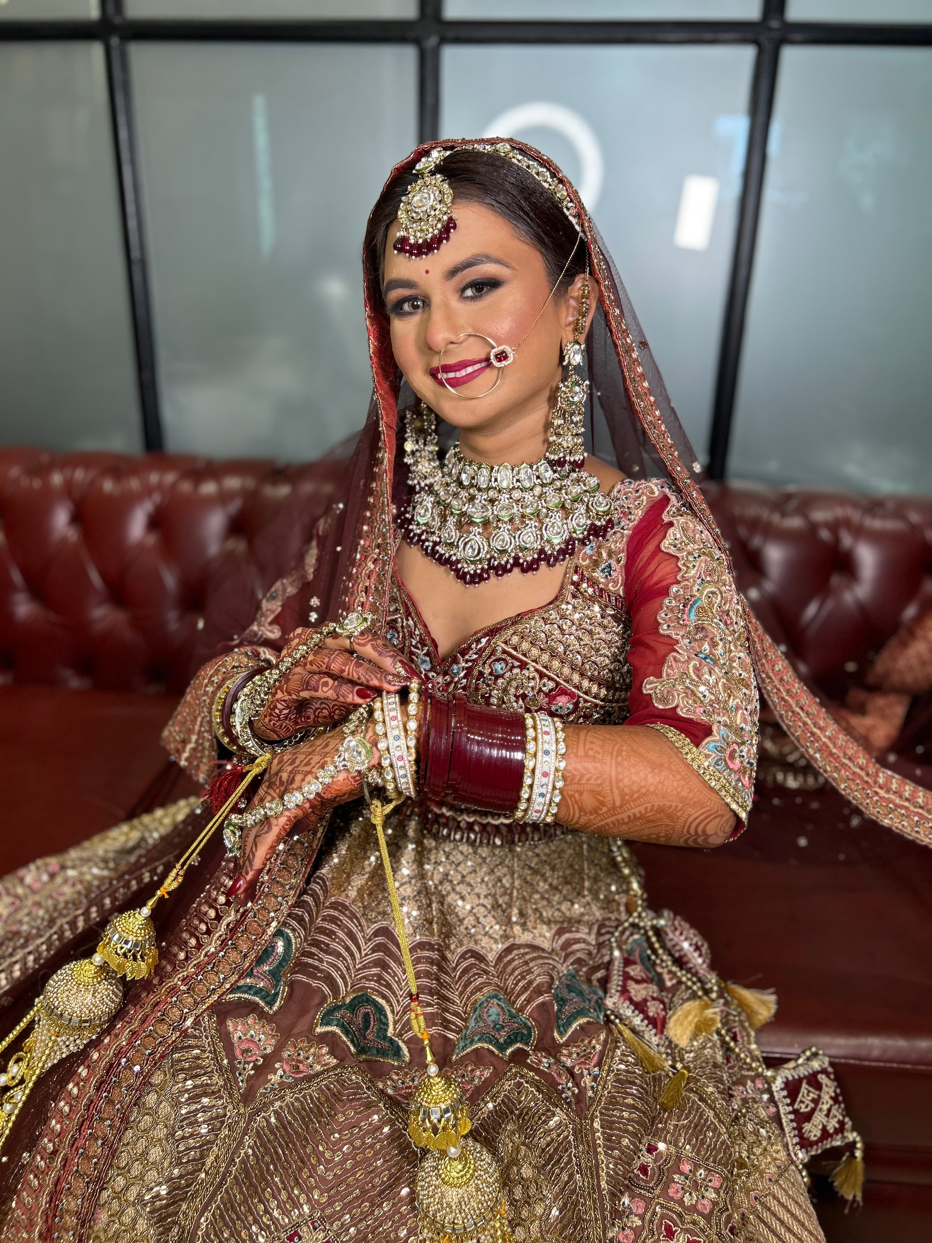A bride seated in maroon and gold with her chooda and kaleere