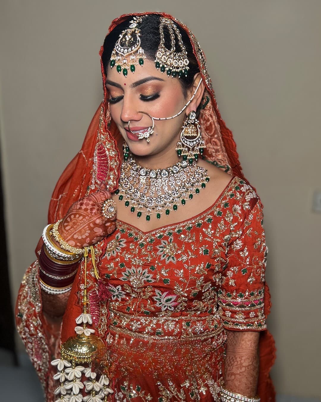 A bride in a rust chunni with emerald kundan and a jasmine kalira
