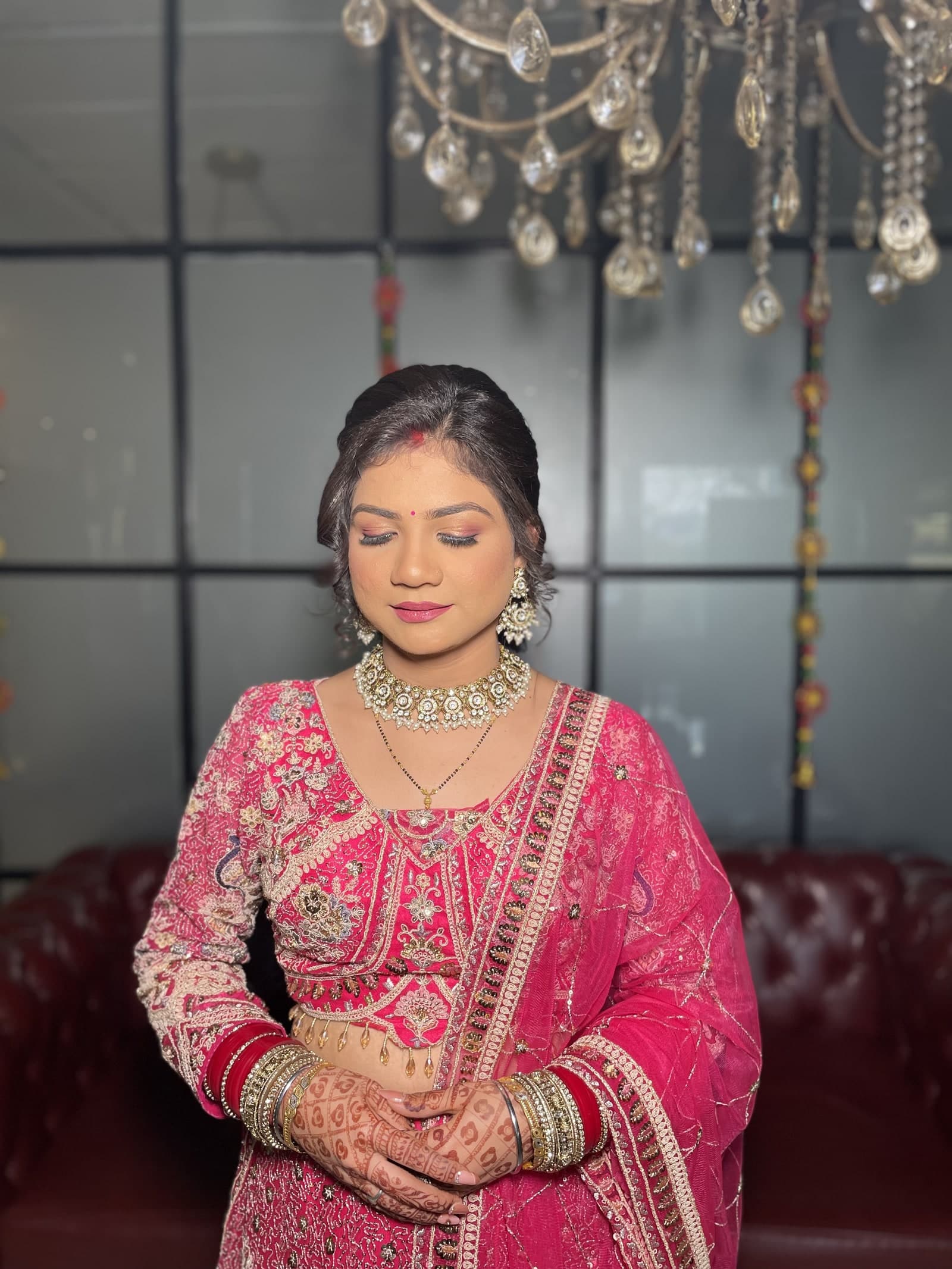 A bride in a rose pink lehenga beneath the studio chandelier